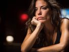 A woman appearing mentally fatigued sits at a casino gaming table, resting her chin on her hand, reflecting the toll of long poker or blackjack sessions