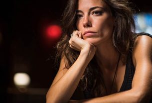 A woman appearing mentally fatigued sits at a casino gaming table, resting her chin on her hand, reflecting the toll of long poker or blackjack sessions