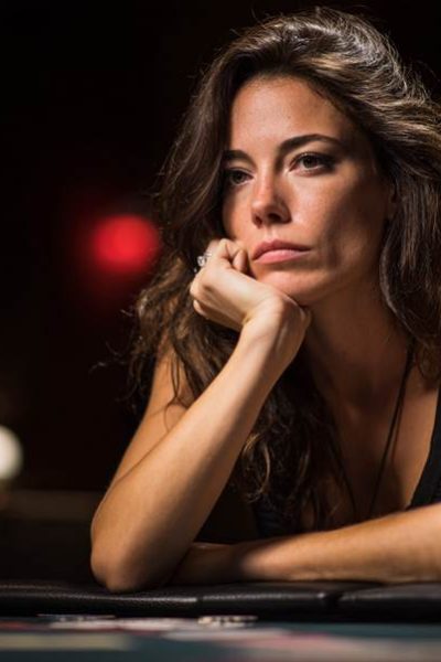 A woman appearing mentally fatigued sits at a casino gaming table, resting her chin on her hand, reflecting the toll of long poker or blackjack sessions